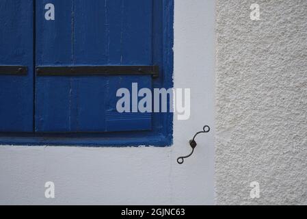 Vecchia casa rurale finestra con persiane di legno blu, cerniere in ferro forgiato e un antico cane otturatore su una parete testurizzata imbiancata in Galaxidi Grecia. Foto Stock
