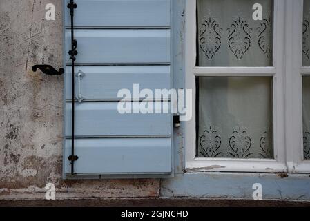 Vecchia casa rurale finestra con tende in pizzo, persiane di legno blu chiaro e un cane con otturatore in ferro forgiato su una parete meteorologica in Galaxidi, Phocis Grecia. Foto Stock