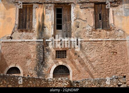 Antica facciata abbandonata con un muro intemperiato e persiane in legno antico a Galaxidi, Phocis Grecia. Foto Stock