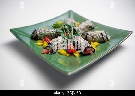 primo piano di involtini di melanzane con formaggio o verdure su piatto su sfondo bianco Foto Stock