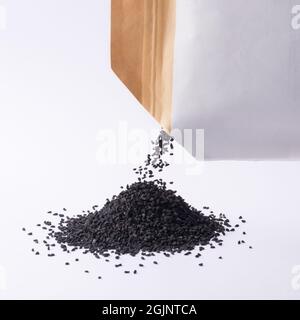 mucchio di semi neri, noti anche come cumino nero o cumino o kalonji, versato fuori da un pacchetto, modello mockup, isolato su sfondo neutro, vicino Foto Stock