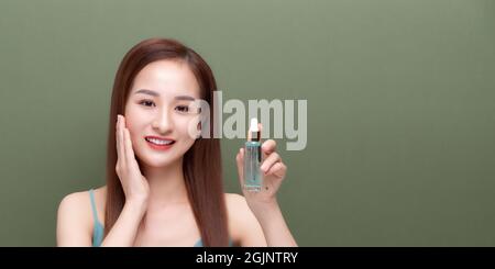 Bella giovane donna che applica siero sulla sua pelle contro sfondo di colore Foto Stock