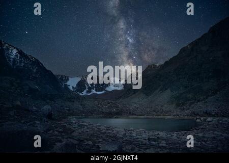 Via lattiginosa e cielo stellato notturno al lago di montagna con vette innevate Foto Stock
