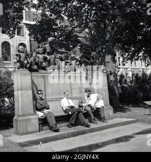 1960, storico, estivo e tre uomini seduti sul sedile della scultura commemorativa Margaret MacDonald, uno leggendo un giornale, nella piazza pubblica o giardino al Lincoln's Inn Fields, Londra, Inghilterra, Regno Unito. Foto Stock