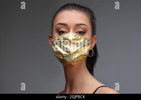 aumento di prezzo di maschere facciali e scarsità in COVID-19 volte concetto come una bella giovane donna che indossa una maschera facciale in oro perché può permetterselo Foto Stock