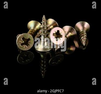 Un mucchio di viti gialle su sfondo nero con riflessi Foto Stock