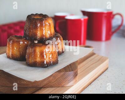 Caneles de Bordeaux su un asse di legno. Famosa pasticceria francese. Accompagnamento con tazza di caffè o tè Foto Stock