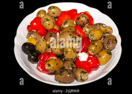 Olive sott'aceto con peperoni ripieni in un piatto bianco, isolate su sfondo nero Foto Stock