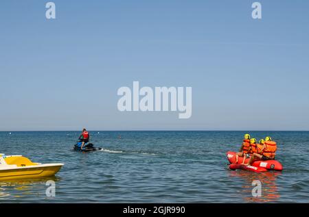 Una famiglia di due adulti e due bambini che si divertono su un gommone trainato sul mare da una moto d'acqua in una soleggiata giornata estiva, Marina di Castagneto Carducci Foto Stock