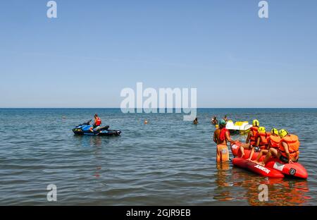 Una famiglia di quattro persone che si divertono su un gommone trainato sul mare da una moto d'acqua in una soleggiata giornata estiva, Marina di Castagneto Carducci, Livorno, Toscana Foto Stock