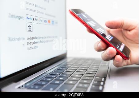 Rottweil, Germania. 9 settembre 2021. Un uomo tiene il suo smartphone per l'autenticazione a due fattori, mentre lo schermo di un laptop visualizza vari metodi di pagamento. Credit: Silas Stein/dpa/Alamy Live News Foto Stock