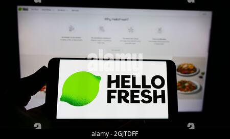 Persona che tiene uno smartphone con il logo della società tedesca di Meal-kit HelloFresh se sullo schermo di fronte al sito web. Mettere a fuoco sul display del telefono. Foto Stock