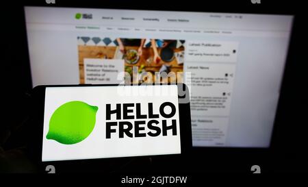 Persona che tiene il cellulare con il logo della società tedesca di Meal-kit HelloFresh se sullo schermo di fronte al sito web aziendale. Mettere a fuoco sul display del telefono. Foto Stock