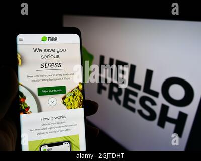 Persona che tiene lo smartphone con il sito web della società tedesca di Meal-kit HelloFresh se sullo schermo di fronte al logo. Concentrarsi sul centro del display del telefono. Foto Stock