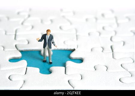 Fotografia di personaggi giocattolo in miniatura. Un uomo d'affari che si sta levando sopra il pezzo mancante di puzzle. Foto immagine Foto Stock