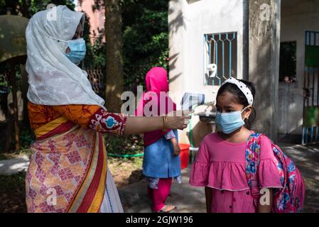 Dhaka, Dhaka, Bangladesh. 12 settembre 2021. Un funzionario controlla la temperatura corporea di uno studente al suo arrivo alla scuola di Dhaka. Il governo del Bangladesh ha revocato le restrizioni alle istituzioni educative dopo 18 mesi di arresti a causa della pandemia del coronavirus Covid-19. (Credit Image: © Fatima-Tuj Johora/ZUMA Press Wire) Foto Stock