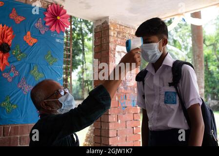 Dhaka, Dhaka, Bangladesh. 12 settembre 2021. Un funzionario controlla la temperatura corporea di uno studente al suo arrivo alla scuola di Dhaka. Il governo del Bangladesh ha revocato le restrizioni alle istituzioni educative dopo 18 mesi di arresti a causa della pandemia del coronavirus Covid-19. (Credit Image: © Fatima-Tuj Johora/ZUMA Press Wire) Foto Stock