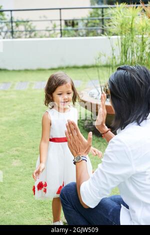 Padre e figlia allegra che stringe le mani quando giocano nel cortile Foto Stock