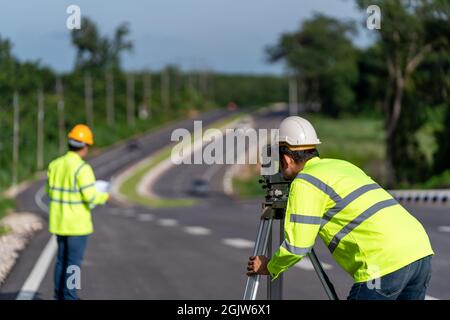 Lavoro di gruppo di tecnici addetti ai topografi che effettuano misurazioni con apparecchiature per strumenti in teodolite durante lavori stradali di costruzione, ingegneri civili, Surveyor Foto Stock