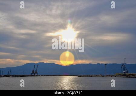 Gru industriali sul molo della città di Rijeka, montagna sullo sfondo. Tramonto sulla città urbana. Foto Stock