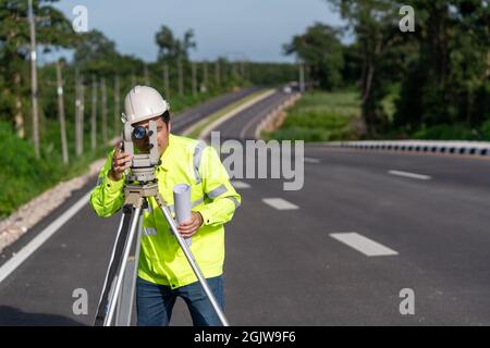 Tecnico di topografia asiatico che effettua la misurazione con teodolite su lavori stradali. Tecnico di topografia in cantiere, attrezzature Surveyor. Foto Stock