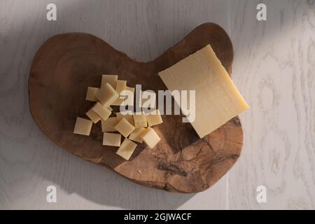 Piccolo blocco di formaggio stagionato affettato in piccoli pezzi su tavola di legno, poco profondo fuoco Foto Stock