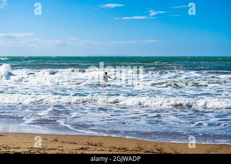 Un surfista che nuota alle onde con la sua tavola da surf, nel golfo di Baratti, Piombino, provincia di Livorno, Italia. Foto Stock