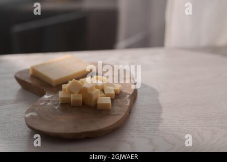 Piccolo blocco di formaggio stagionato affettato in piccoli pezzi su tavola di legno, poco profondo fuoco Foto Stock