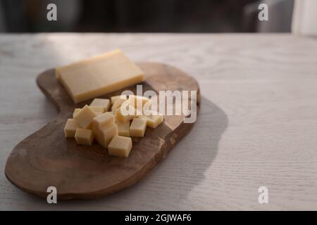Piccolo blocco di formaggio stagionato affettato in piccoli pezzi su tavola di legno, poco profondo fuoco Foto Stock