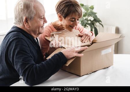 Felice coppia senior disimballaggio consegna scatola di cartone in casa - Focus sul volto donna Foto Stock