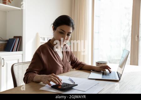 Focalizzata giovane indiana femmina calcolare utility prima di effettuare il pagamento online Foto Stock