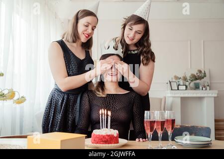 Due ragazze hanno preparato una scatola del regalo imballata per il loro amico di compleanno, chiudendo gli occhi con le mani, celebrando la giornata delle donne, avendo i vetri con lo champagne Foto Stock