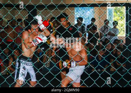 Un arbitro guardò due combattenti MMA (Mixed Martial Arts) che stavano combattendo nel campionato e il pubblico guardò da dietro le gabbie di filo. Foto Stock