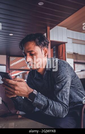 Un bel maschio indiano in una camicia utilizzando uno smartphone Foto Stock