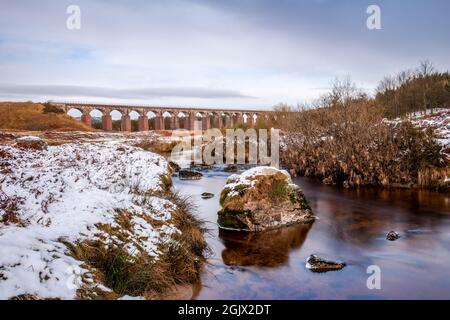 Lunga esposizione della Grande acqua della flotta circondata dalla neve in inverno, con il viadotto ferroviario sullo sfondo, Dumfries e Galloway, Scozia Foto Stock