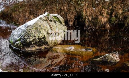 Un rastrello di bronzo attaccato ad un grande masso da una catena, coperta di neve in inverno, sulla Grande acqua del fiume Fleet al viadotto ferroviario, Galloway, SCO Foto Stock