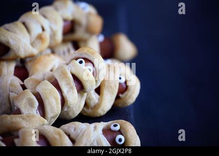 Cibo divertente per i bambini. Gruppo di hot dog mummy su un tavolo rustico blu. Messa a fuoco selettiva con primo piano e sfondo sfocati. Foto Stock