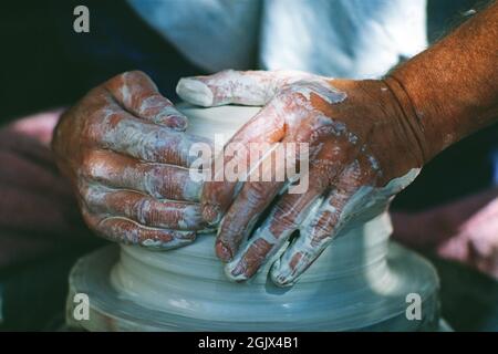 Primo piano delle mani dell'uomo gettando una pentola sulla ruota di un vasaio. Foto Stock