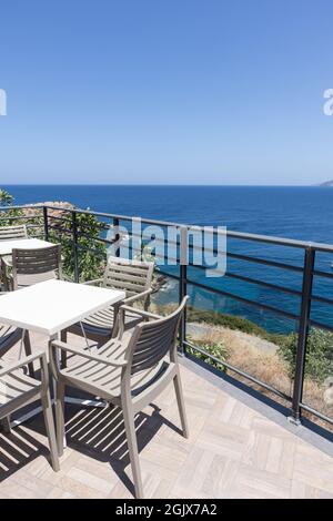 Sedie e tavoli vuoti in plastica in un bar all'aperto su un balcone con vista sul mare Foto Stock