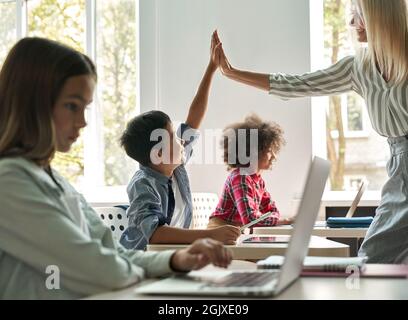 Buon insegnante che dà alto cinque a ragazzo in classe con gruppo di scolari. Foto Stock