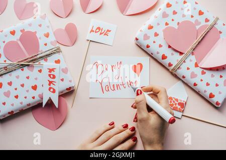 Donna firma una cartolina San Valentino ESSERE IL MIO SAN VALENTINO. Decorazioni e regali d'amore per le feste. Foto Stock