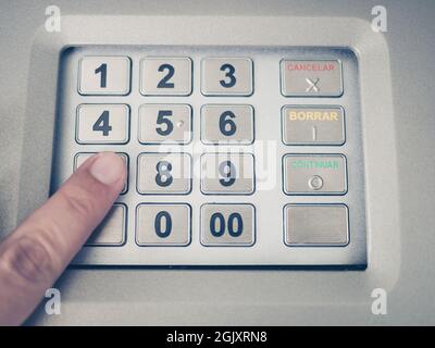 Un primo piano di una mano di un uomo che preme il codice numerico su una macchina ATM Foto Stock