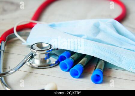 provetta per analisi del sangue del virus corona, stetoscopio e maschera sul tavolo Foto Stock
