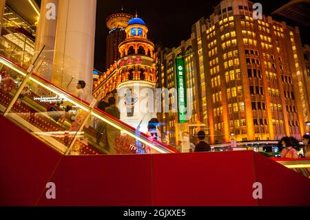 Gli acquirenti salgono la scala mobile presso l'edificio Shimao sulla strada pedonale Nanjing East Road nel centro di Shanghai, Cina, di notte. Foto Stock