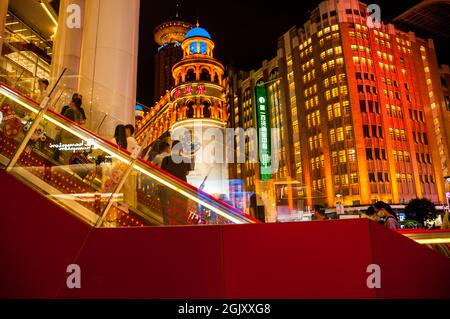 Gli acquirenti salgono la scala mobile presso l'edificio Shimao sulla strada pedonale Nanjing East Road nel centro di Shanghai, Cina, di notte. Foto Stock