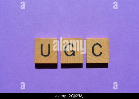 UGC, acronimo di User Generated Content in wooden alfabet letters isolato su sfondo viola Foto Stock