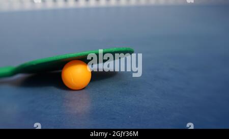 Paddle da ping pong verde con palla arancione appoggiata sul tavolo in attesa di una partita Foto Stock