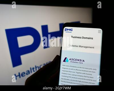 Persona che tiene il cellulare con la pagina web della società giapponese PHC Holdings Corporation sullo schermo di fronte al logo. Concentrarsi sul centro del display del telefono. Foto Stock