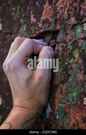 Primo piano di una mano calciosa di un arrampicatore che afferra una piccola presa su una roccia. Foto Stock