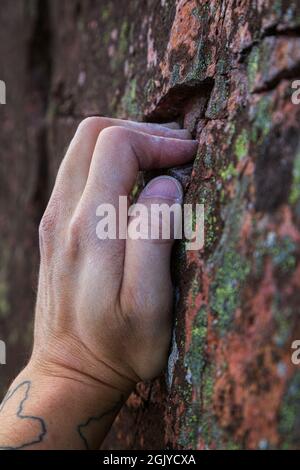 Primo piano di una mano calciosa di un arrampicatore che afferra una piccola presa su una roccia. Foto Stock